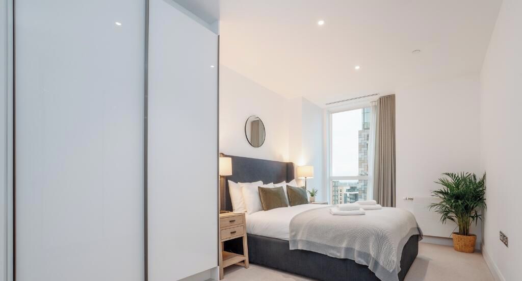 Een moderne hotelkamer met een groot bed, nachtkastjes, een potplant en uitzicht op de stad.
