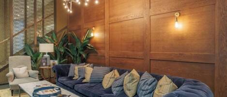Una sala de estar moderna con un sofá azul oscuro, una mesita de centro y una lámpara. Se aprecia un panel de pared de madera y una planta al fondo.
