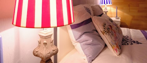 Habitación de hotel con cama, mesita de noche, lámpara, equipo de aire acondicionado, ventana y un cuadro colgado en la pared.