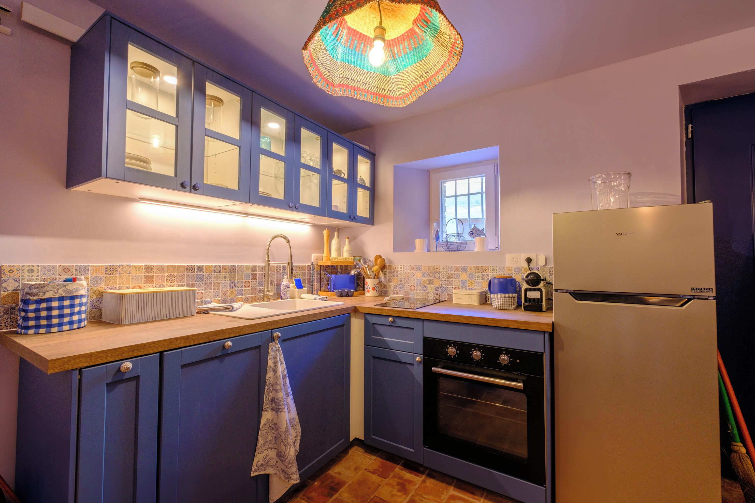 Una cocina con armarios azules, un refrigerador blanco y una lámpara colgante de colores.