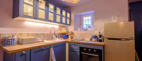 Una cocina con armarios azules, un refrigerador blanco y una lámpara colgante de colores.