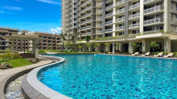 A swimming pool with a curved edge, surrounded by a building with multiple balconies and a covered area with lounge chairs. - 3 Bedroom Condo near BGC Taguig Alder Residences (Taguig)
