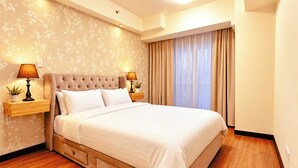 Habitación de hotel con una cama grande, dos mesitas de noche con lámparas, suelo de madera y un diseño de papel tapiz floral.