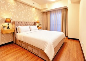 A hotel room with a large bed, two bedside tables with lamps, a wooden floor, and a floral wallpaper design. - 3 Bedroom Condo near BGC Taguig Alder Residences (Taguig)