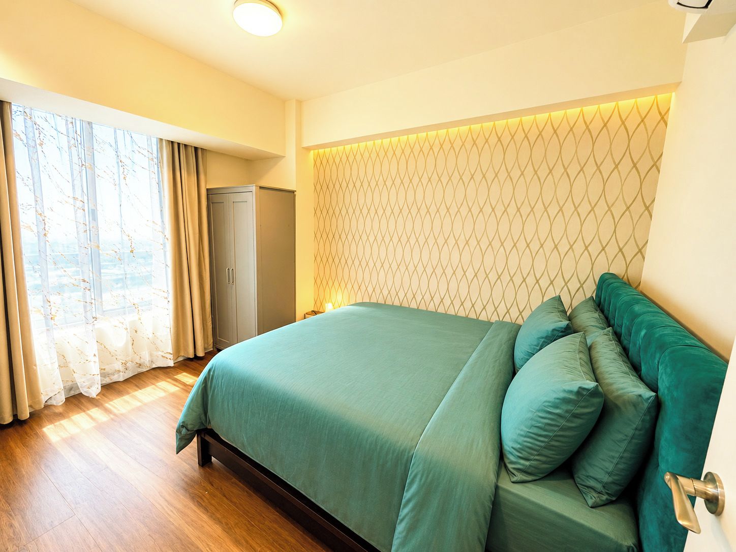 Una habitación de hotel con cama, cortinas, un armario y un papel tapiz estampado.