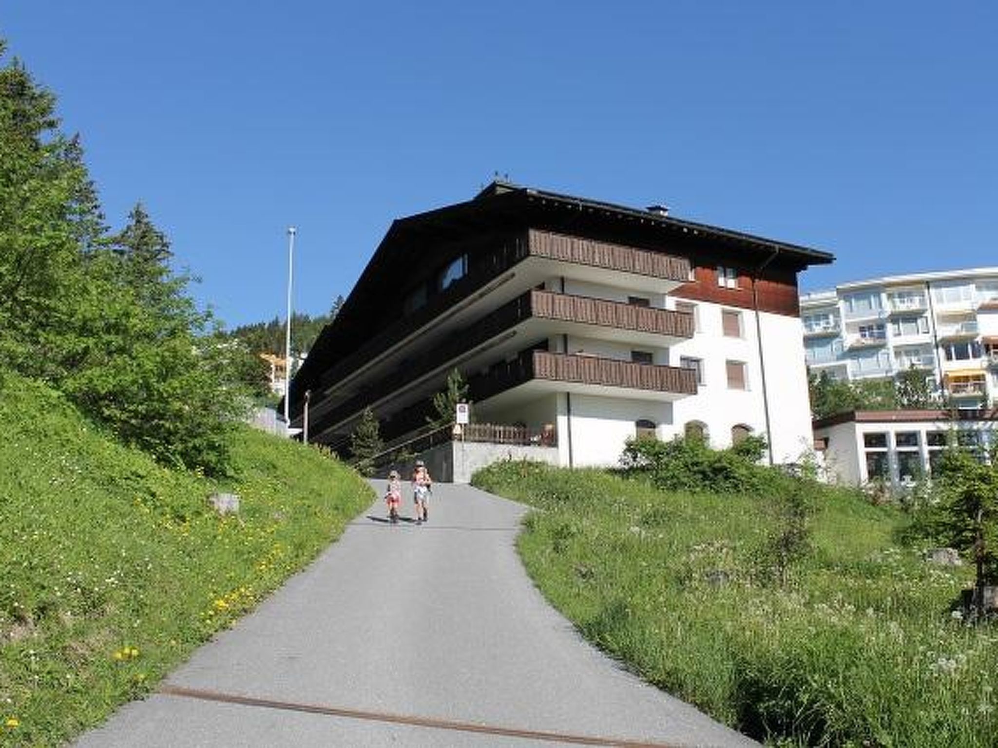 Ein Weg führt zu einem mehrstöckigen Gebäude mit Balkonen, umgeben von Grünpflanzen.