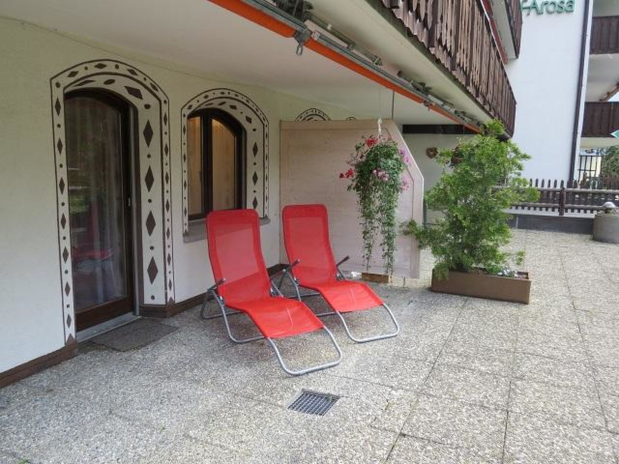 Un bâtiment doté d’un balcon, de deux chaises rouges et d’une plante en pot.