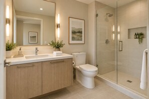 Ein modernes Badezimmer mit Duschkabine aus Glas, Toilette und Waschtisch mit Becken und Spiegel.