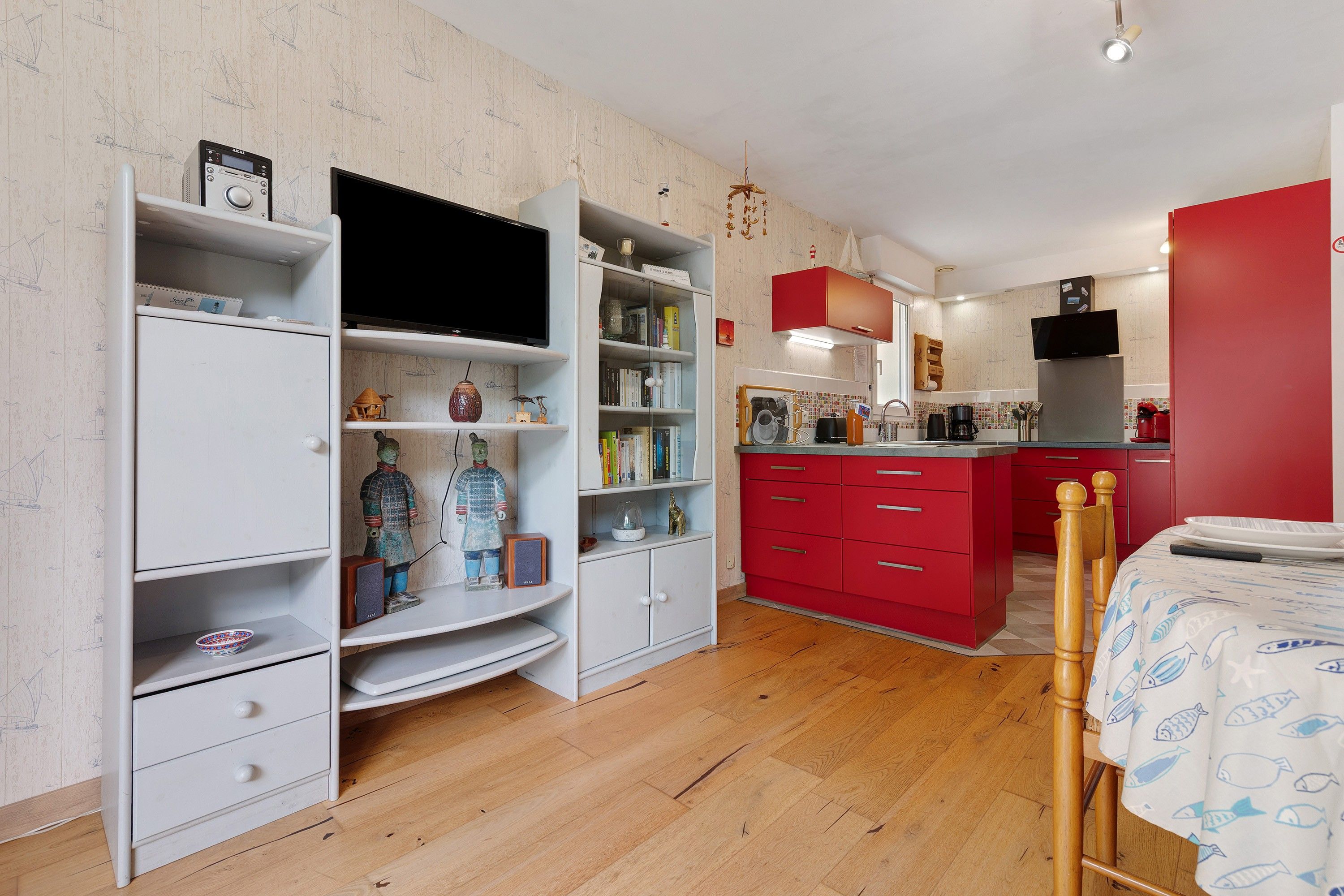 A modern kitchen with red cabinets, a dining area with a wooden table, and a TV mounted on the wall.