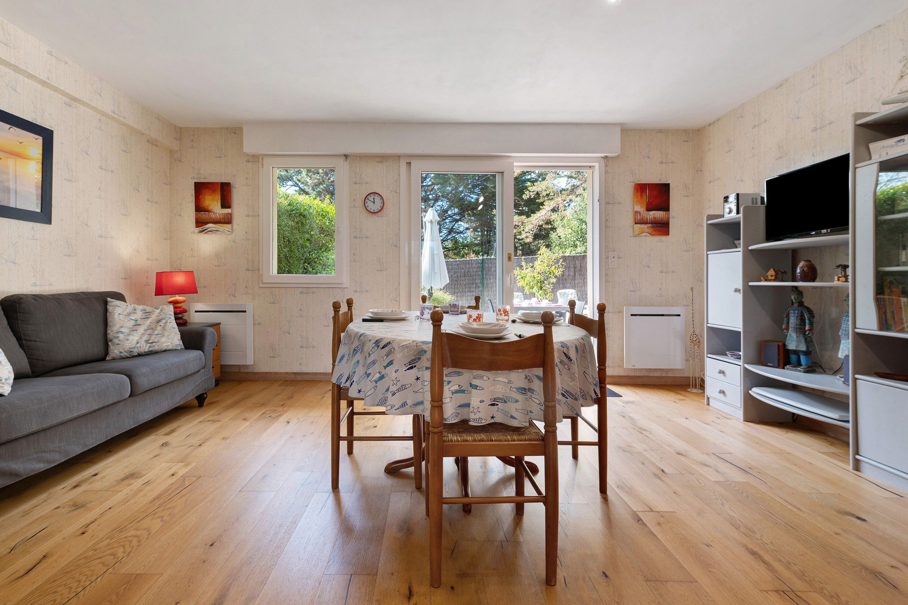 Una sala acogedora con un sofá gris, una mesa de comedor con sillas y un televisor sobre un mueble.