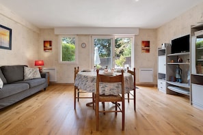 Un salon chaleureux avec un canapé gris, une table à manger avec des chaises et un téléviseur posé sur un meuble.