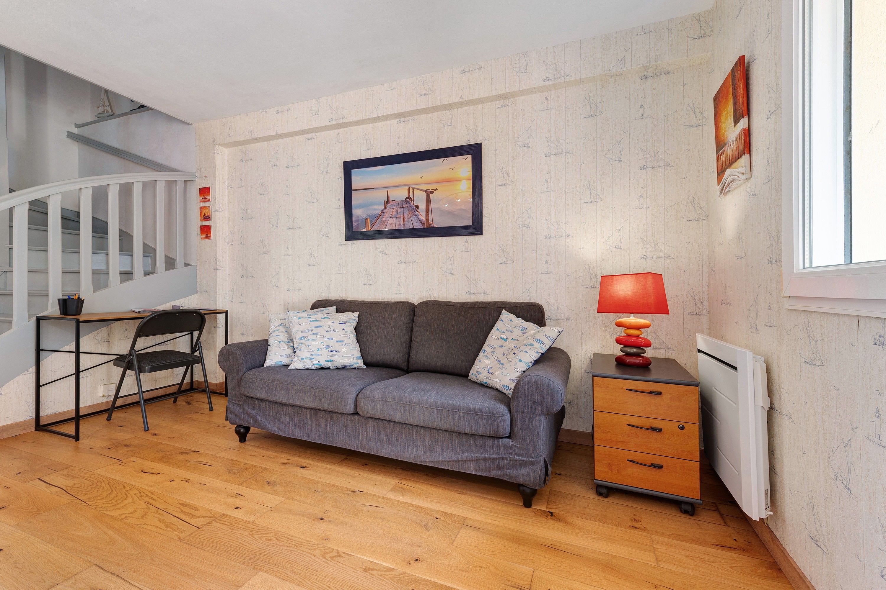 Et møbleret værelse med sofa, skrivebord, stol, lampe og radiator.