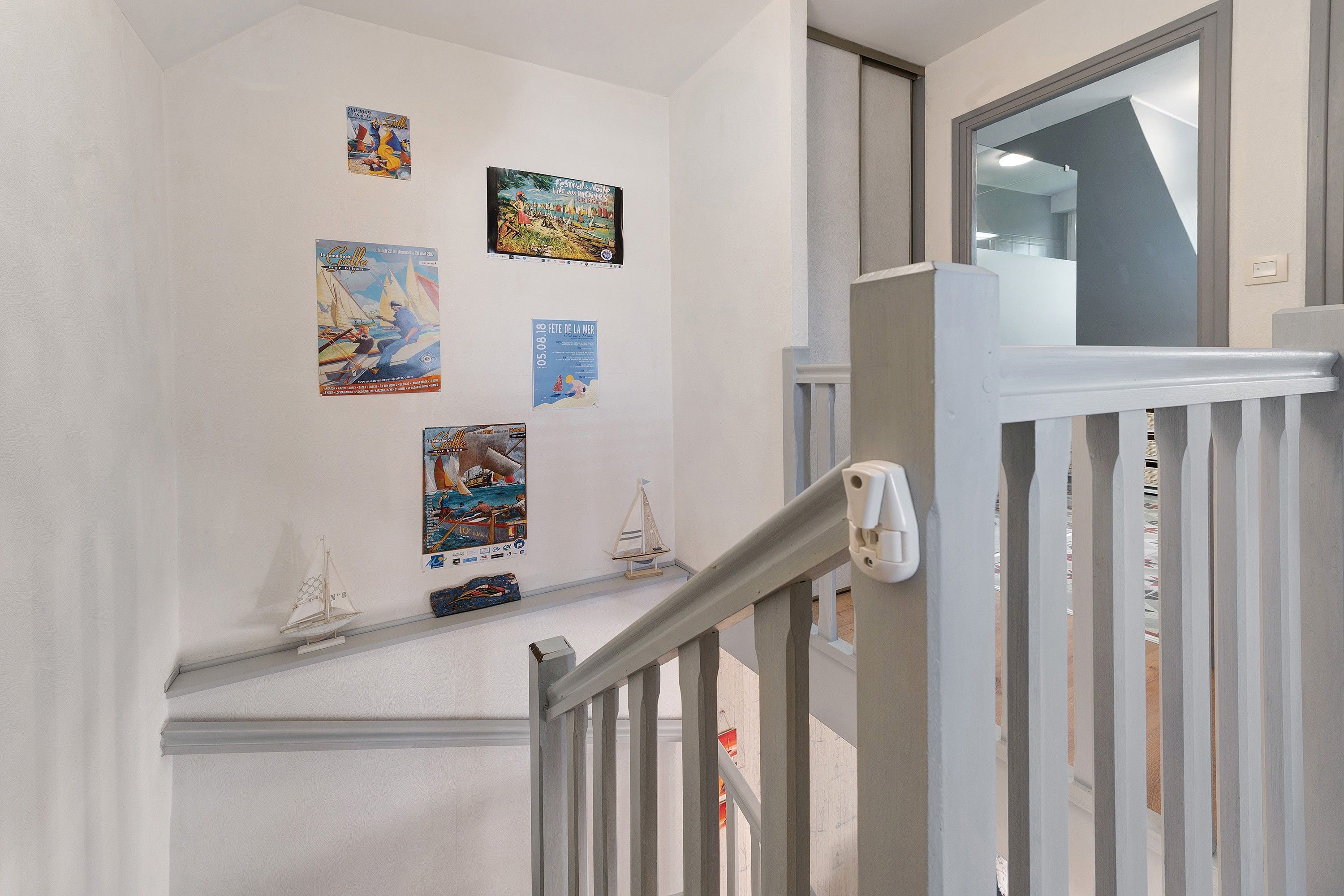 A staircase with a white railing, a small shelf with model ships, and several posters on the wall.