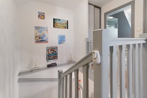 A staircase with a white railing, a small shelf with model ships, and several posters on the wall.