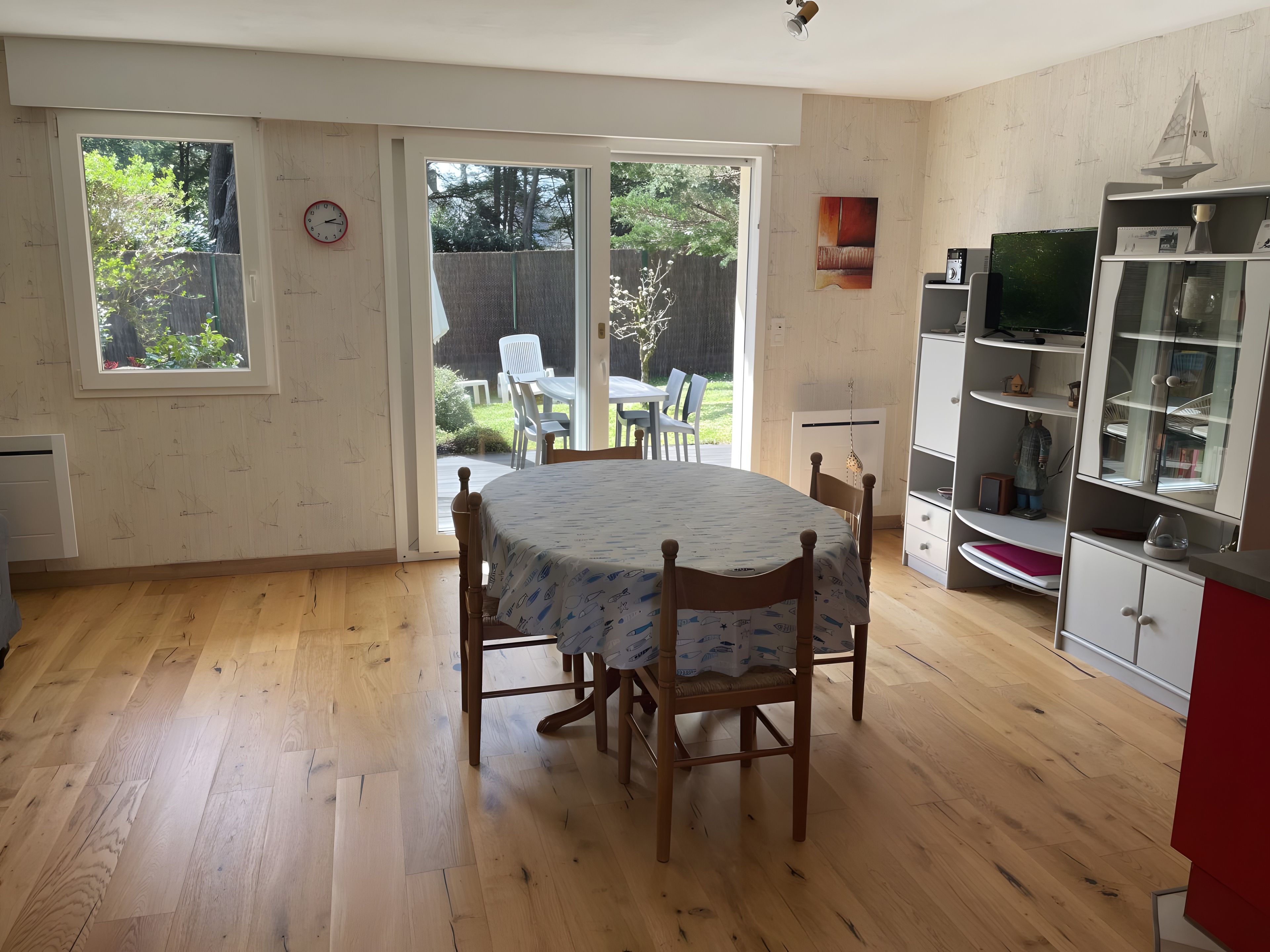 Ein Zimmer mit Holzboden, einem Esstisch mit Stühlen, einer Küchenzeile mit Schränken und einer Glastür zum Außenbereich.