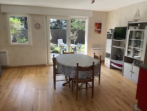 Ein Zimmer mit Holzboden, einem Esstisch mit Stühlen, einer Küchenzeile mit Schränken und einer Glastür zum Außenbereich.