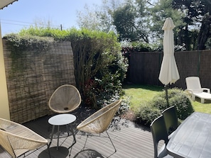 Eine Terrasse mit Korbstühlen und einem Tisch, umgeben von einer Holzdielenveranda und einem Gartenbereich mit Holzzaun und Grünpflanzen.