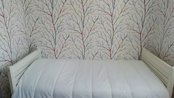 Cama com colchão branco e cabeceira, encostada a parede com papel de parede estampado com padrão de galhos de árvore.