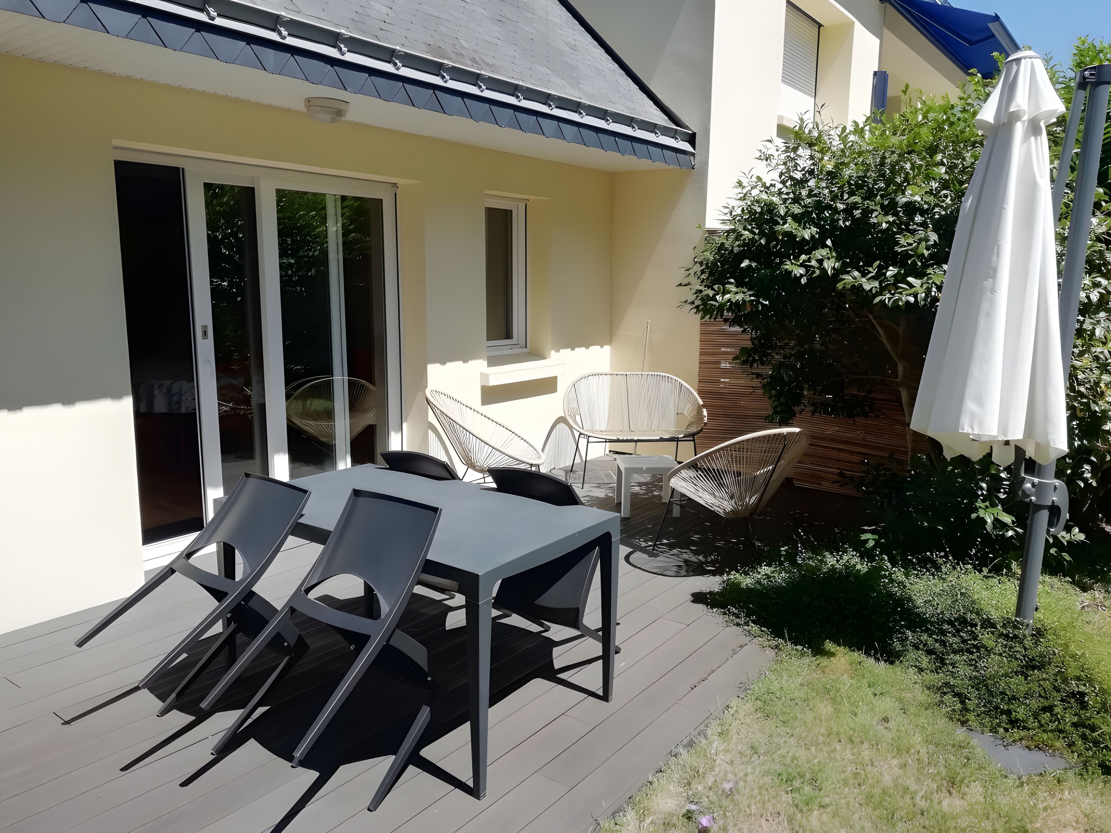 Een terras buiten, met een tafel, stoelen, een witte parasol en een schuifpui.