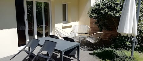 An outdoor patio with a table and chairs, a white umbrella, and a sliding glass door.