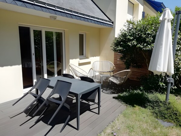 Eine Terrasse im Freien mit Tisch und Stühlen, einem weißen Sonnenschirm und einer Schiebetür.