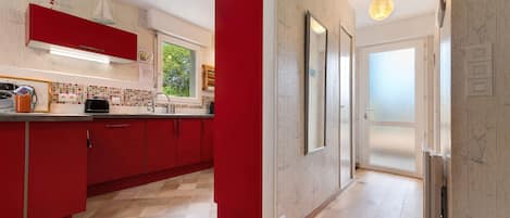 A modern kitchen with red cabinetry, a tiled backsplash, and a wooden floor.