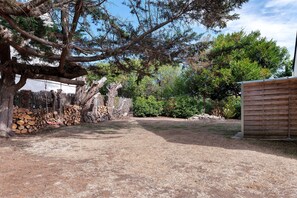 A gravel driveway leading to a wooden building with a fenced area containing stacked firewood.