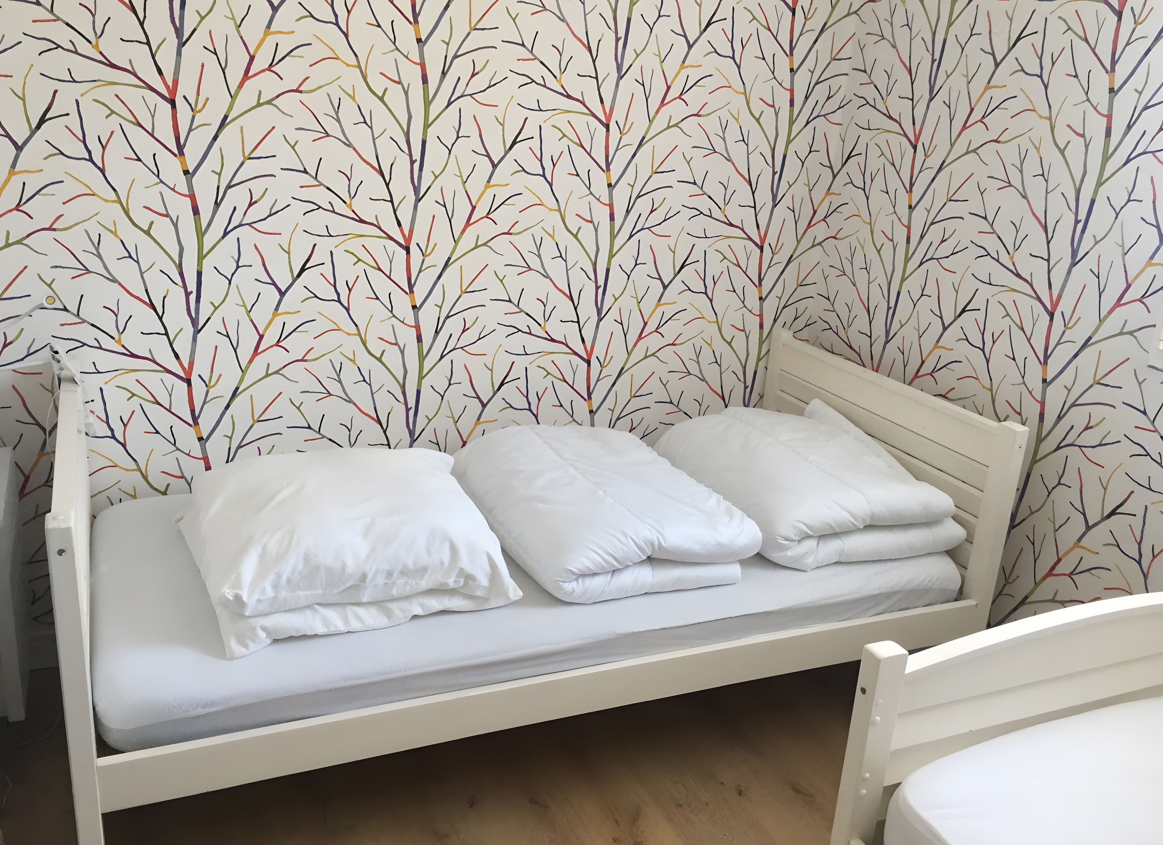 Ein Einzelbett mit weißer Bettwäsche in einem Raum mit Wandpapier mit einem Astmuster.