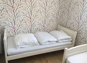 Ein Einzelbett mit weißer Bettwäsche in einem Raum mit Wandpapier mit einem Astmuster.