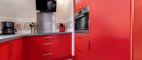 Una cocina con armarios rojos, un refrigerador de acero inoxidable, una cafetera y un microondas.
