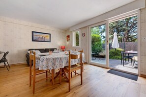 A dining area with a table set for two, a sofa, and a view through a glass door to an outdoor deck.