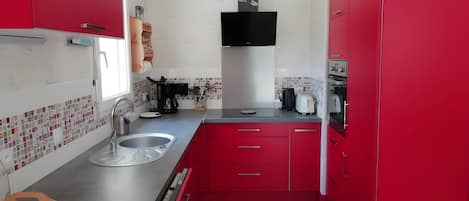 A kitchen with red cabinets, a stainless steel sink, and a flat-screen TV mounted above the counter.