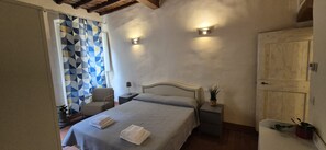 A bedroom with a bed, a chair, a bedside table, a wall-mounted light, and a door. - Charming 2-Bedroom San Frediano Hideaway Near the Ponte Vecchio (Firenze)