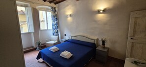 A bedroom with a bed, bedside tables, a window with curtains, and a wall-mounted light fixture. - Charming 2-Bedroom San Frediano Hideaway Near the Ponte Vecchio (Firenze)