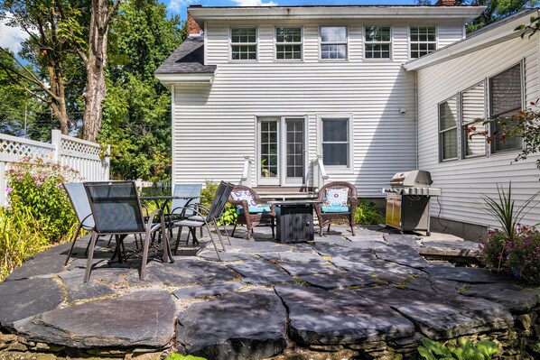 A house with a stone patio, outdoor furniture, and a barbecue grill.