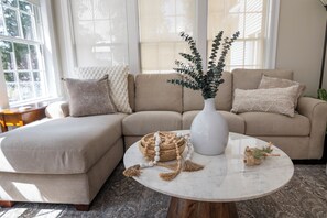 A living room with a sectional sofa, a round coffee table, and a potted plant.