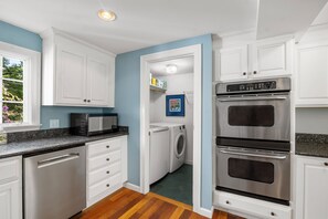 A kitchen with white cabinets, a microwave, an oven, and a washing machine.