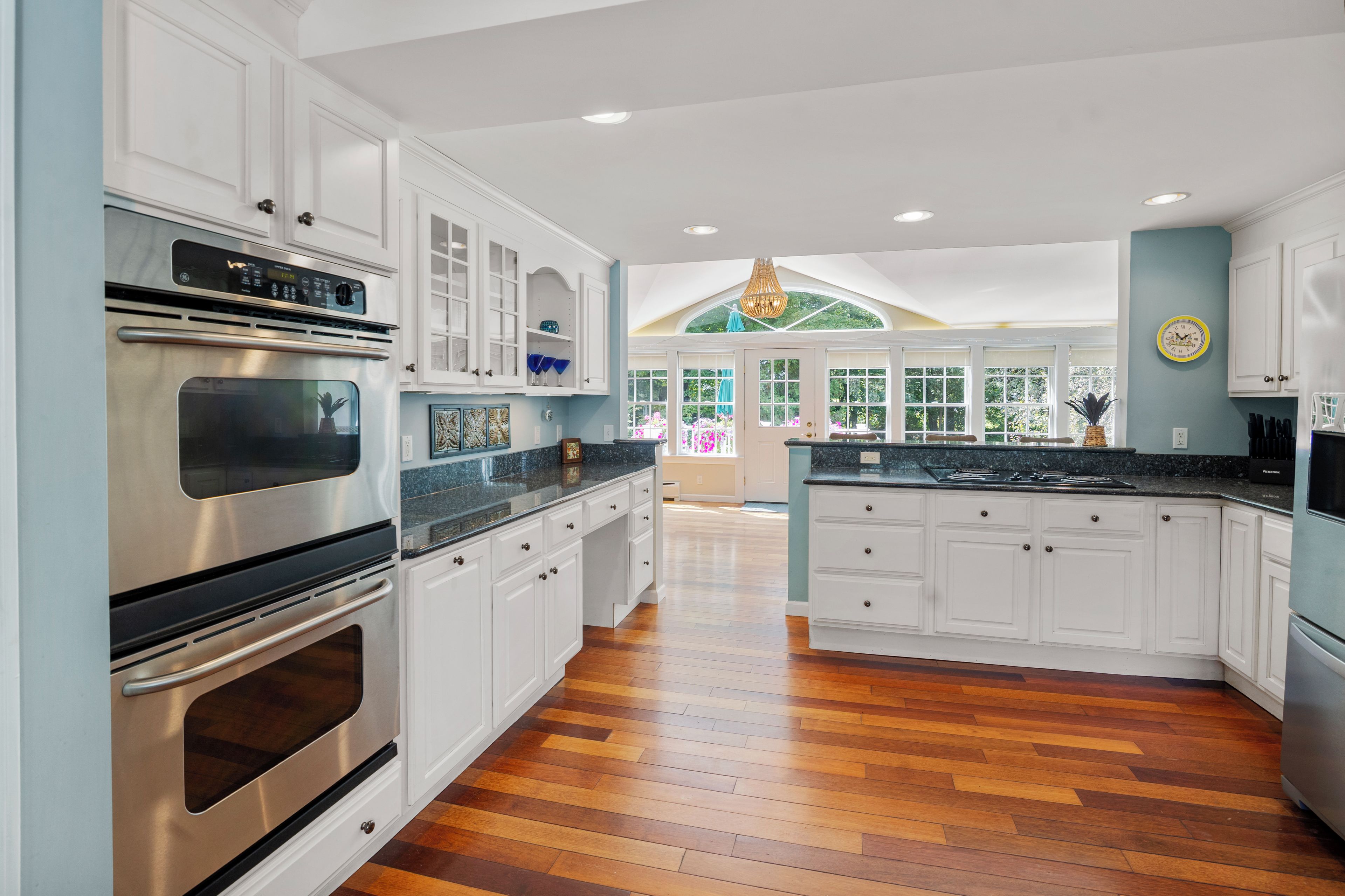A modern kitchen with stainless steel appliances, white cabinetry, and a herringbone wood floor.