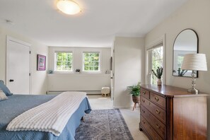 A bedroom with a bed, dresser, windows, and a radiator.