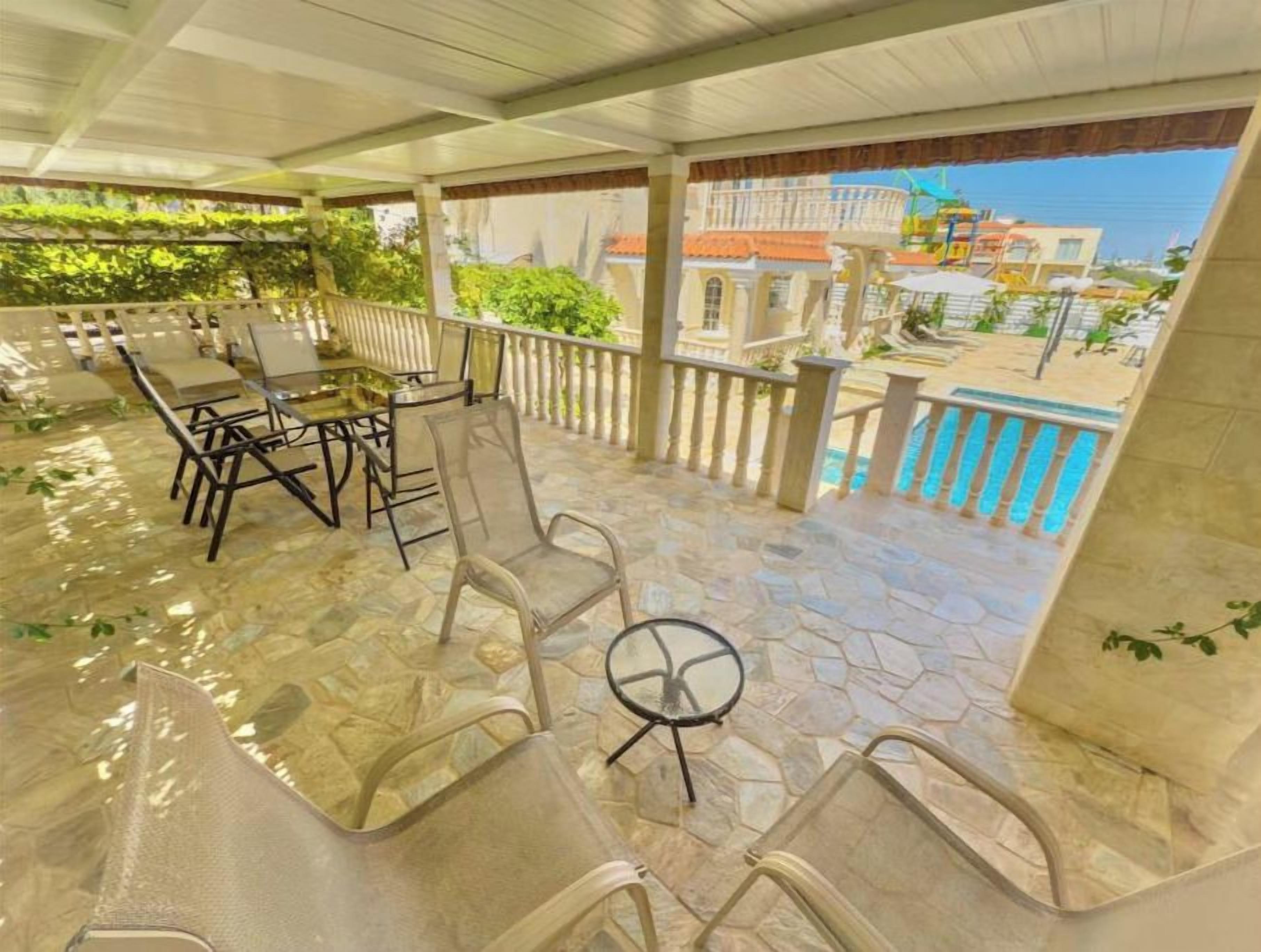 An outdoor patio with stone flooring, metal chairs, and a glass table.