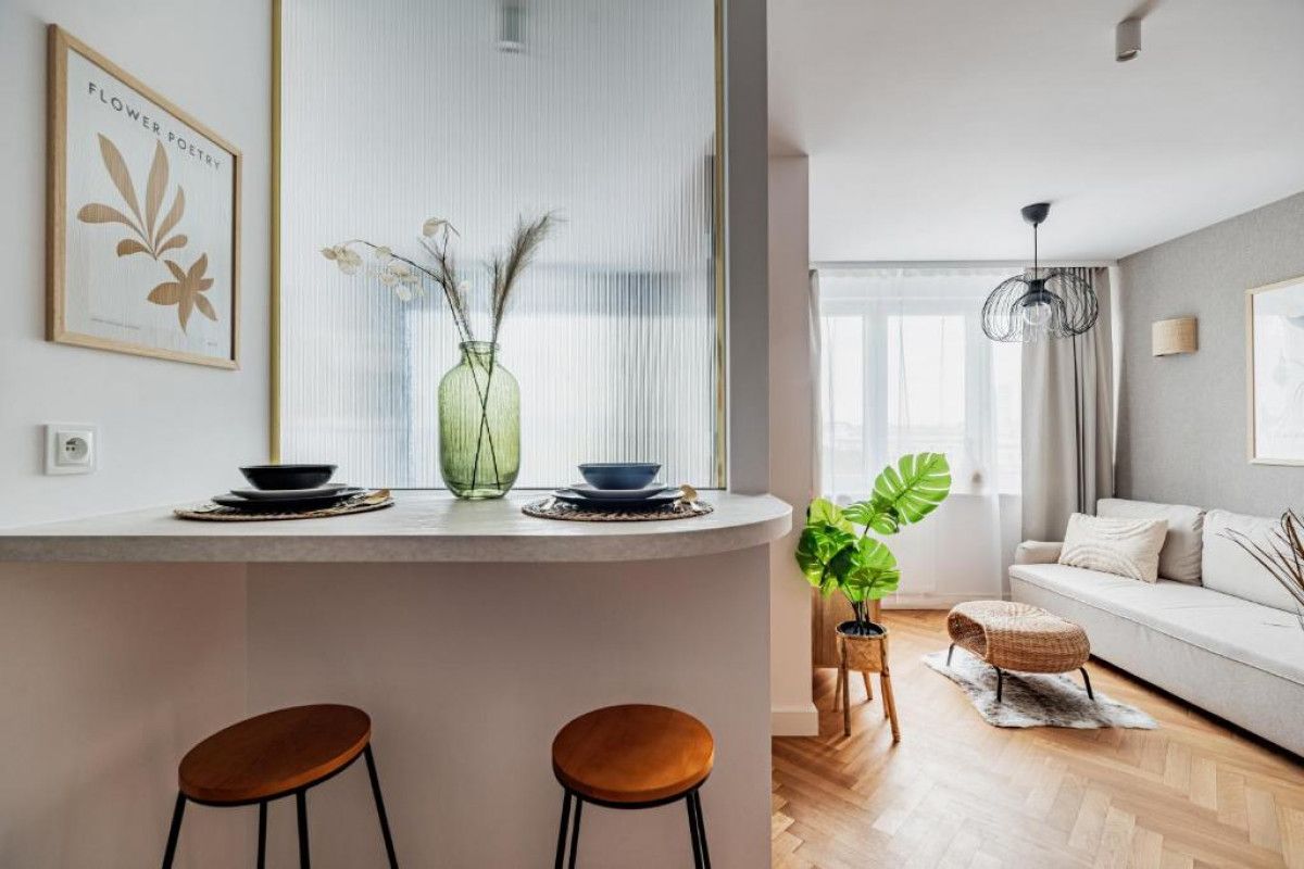 Une cuisine moderne avec un plan de travail blanc, deux tabourets et un vase contenant des plantes séchées.