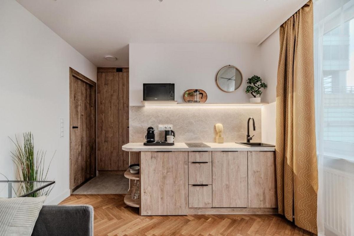 A compact kitchen with a built-in microwave, a coffee maker, and a sink. There is a wooden door leading to another room, and a plant on the counter.