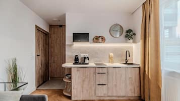 A compact kitchen with a built-in microwave, a coffee maker, and a sink. There is a wooden door leading to another room, and a plant on the counter.
