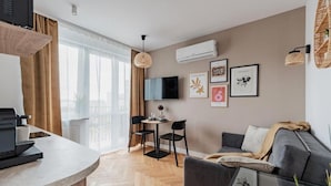 Una sala moderna con sofá, comedor con sillas, televisor de pantalla plana montado en la pared y ventana con cortinas.