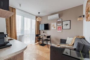 A modern living room with a sofa, a dining area with chairs, a flat-screen TV mounted on the wall, and a window with curtains. - Modern City Centre by Arrenda (Warszawa)