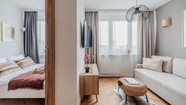Una sala de estar moderna con un sofá, una mesita de madera, un televisor y vistas de la ciudad a través de amplios ventanales.