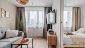 Un dormitorio moderno con cama, mesita de noche, televisor y ventana con cortinas.