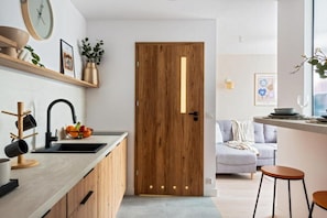 A modern kitchen with a wooden door, a sink, and a countertop with a bowl of fruit. - Modern City Centre by Arrenda (Warszawa)