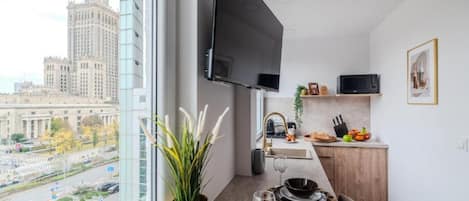 A modern kitchen with a flat-screen TV, a dining area with a table set for two, and a view of a cityscape through large windows.