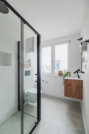 A modern bathroom with a glass shower enclosure, a toilet, and a wooden vanity with a sink. - Modern City Centre by Arrenda (Warszawa)